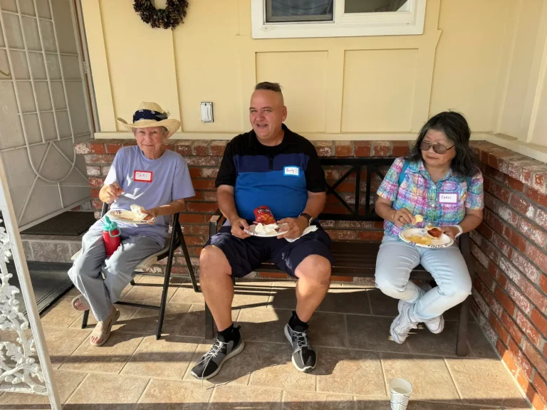 Three supporters wearing name tags share food on a porch at April Chan’s San Leandro meet and greet